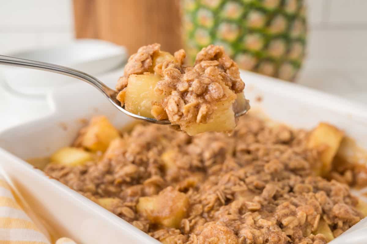 a spoon lifting pineapple crisp from a baking dish.