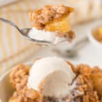 Pineapple crisp in a bowl with a scoop of vanilla ice cream, and a spoon lifting up some.