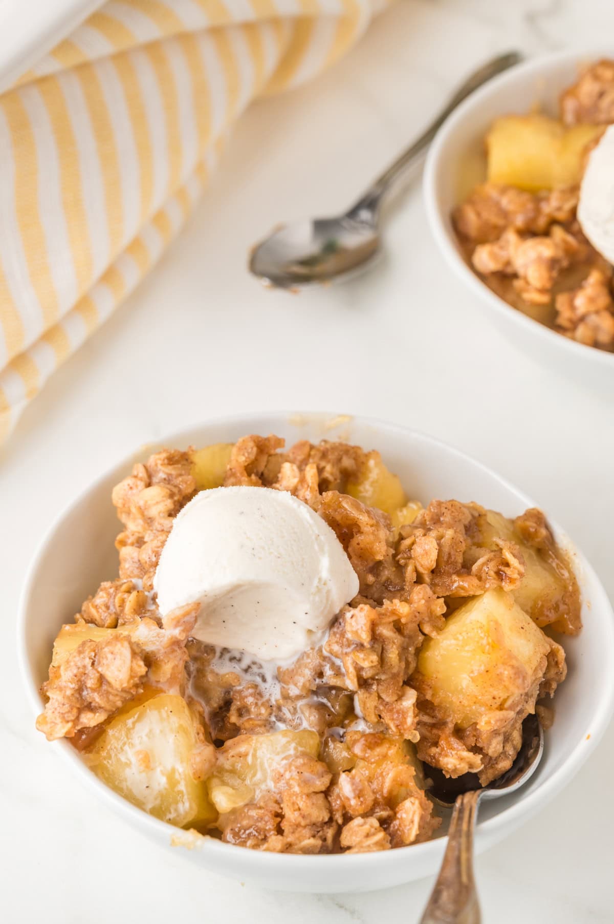 Pineapple crisp in a bowl with a scoop of vanilla ice cream.