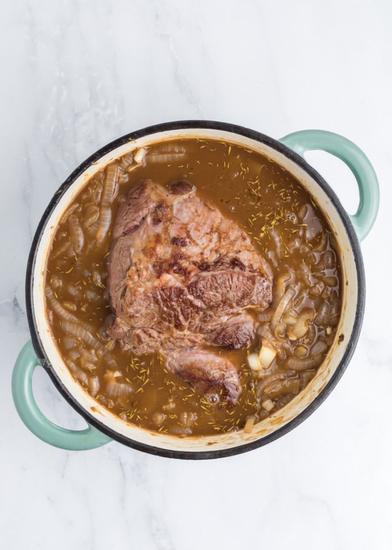 a dutch oven with french onion chuck roast inside.