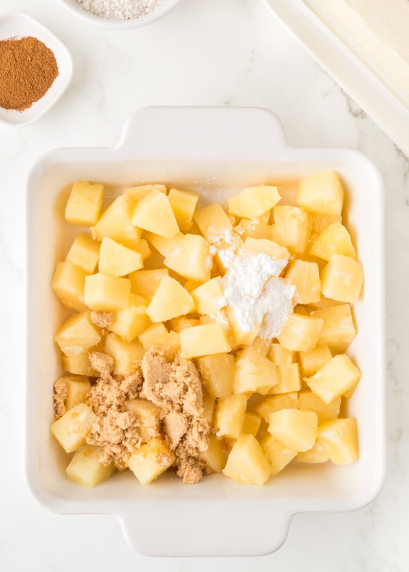 a white baking dish with pineapple chunks and brown sugar in it.