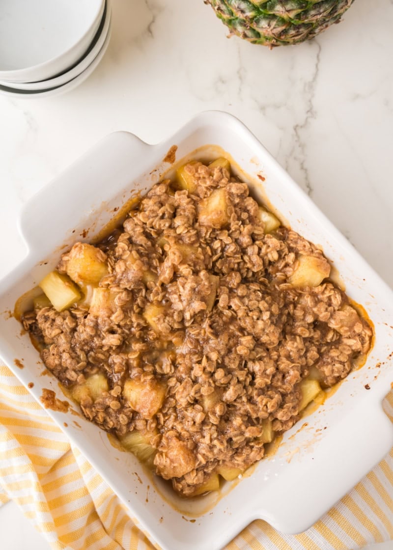 a baking dish of pineapple crisp with a fresh pineapple beside it.
