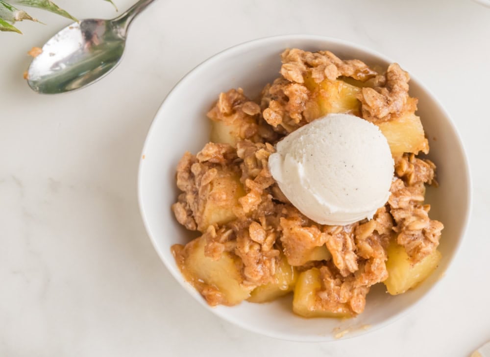 Pineapple crisp in a bowl with a coop of vanilla ice cream.