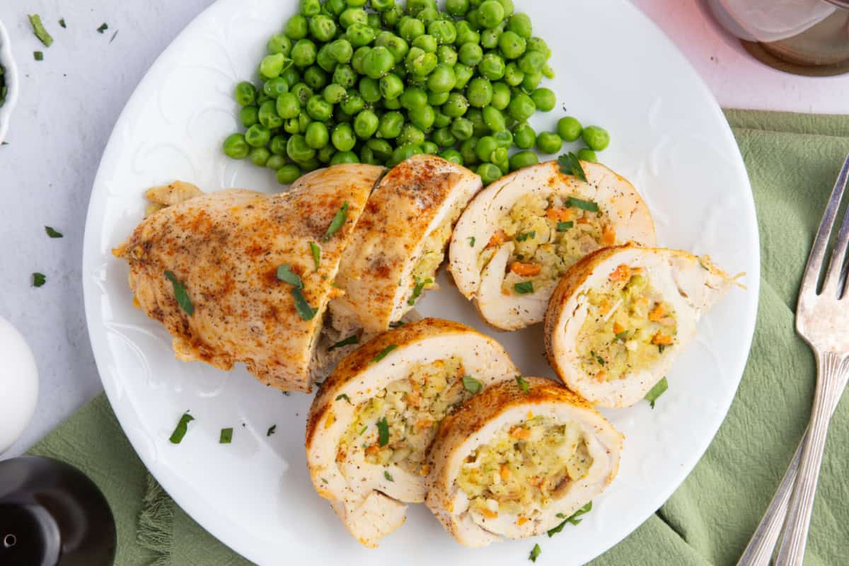 Stuffed chicken breast stuffed with stuffing sliced on a white plate and served with peas.