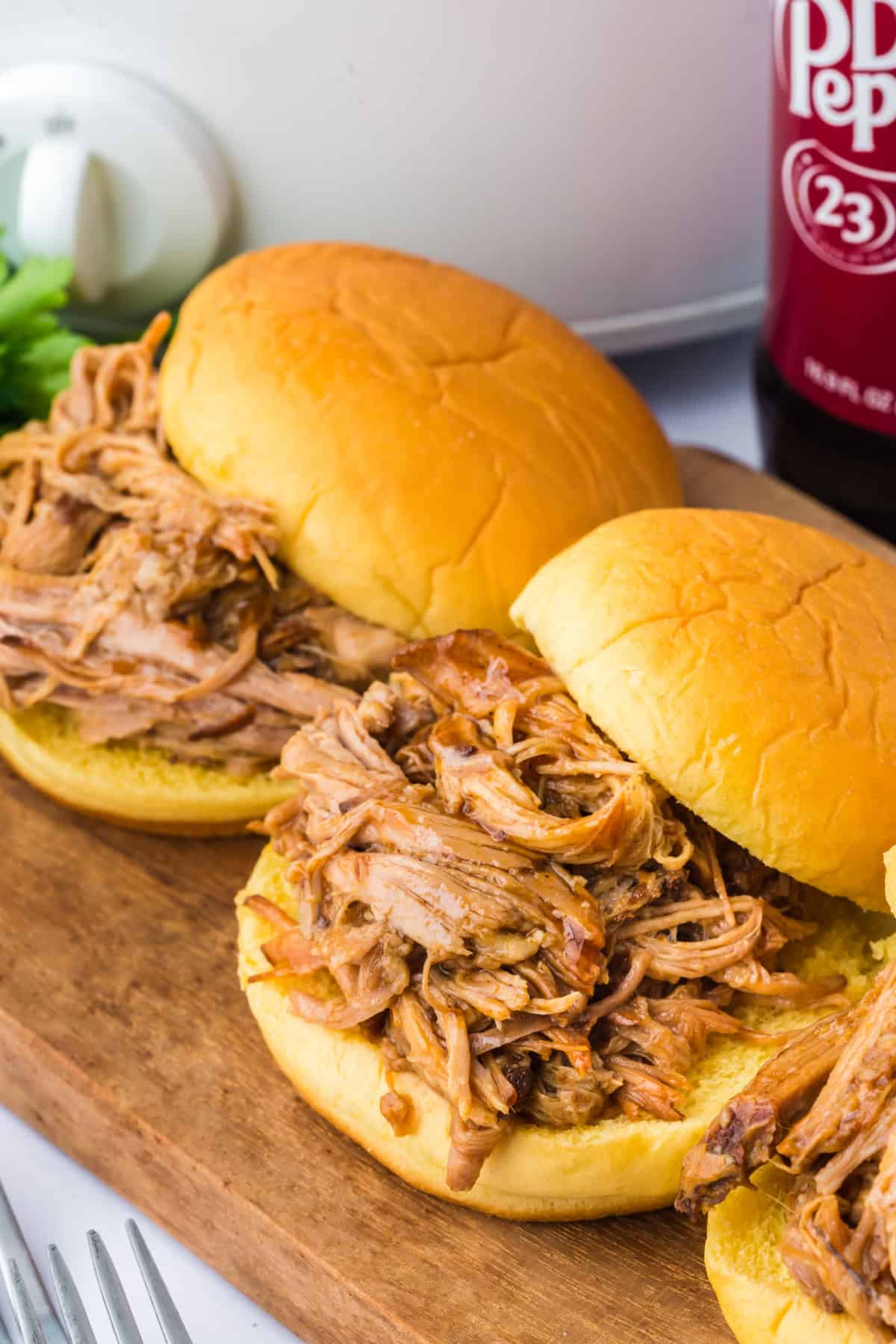 pulled pork on sandwich buns in front of a slow cooker and a bottle of soda.
