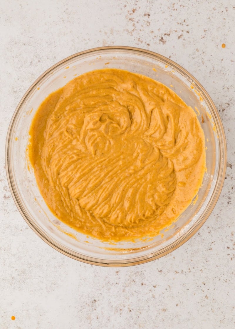 a glass bowl with pumpkin muffin batter inside it.