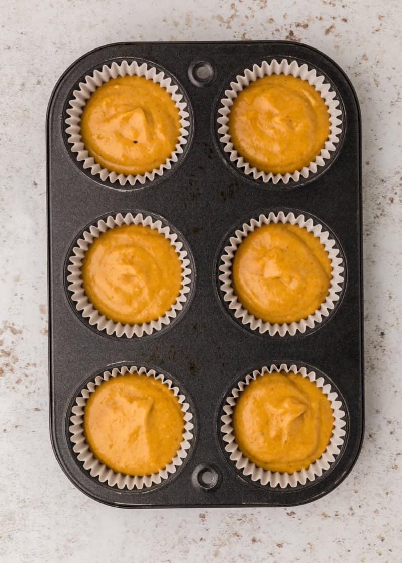 a muffin tin with uncooked batter in the paper liners on a table.