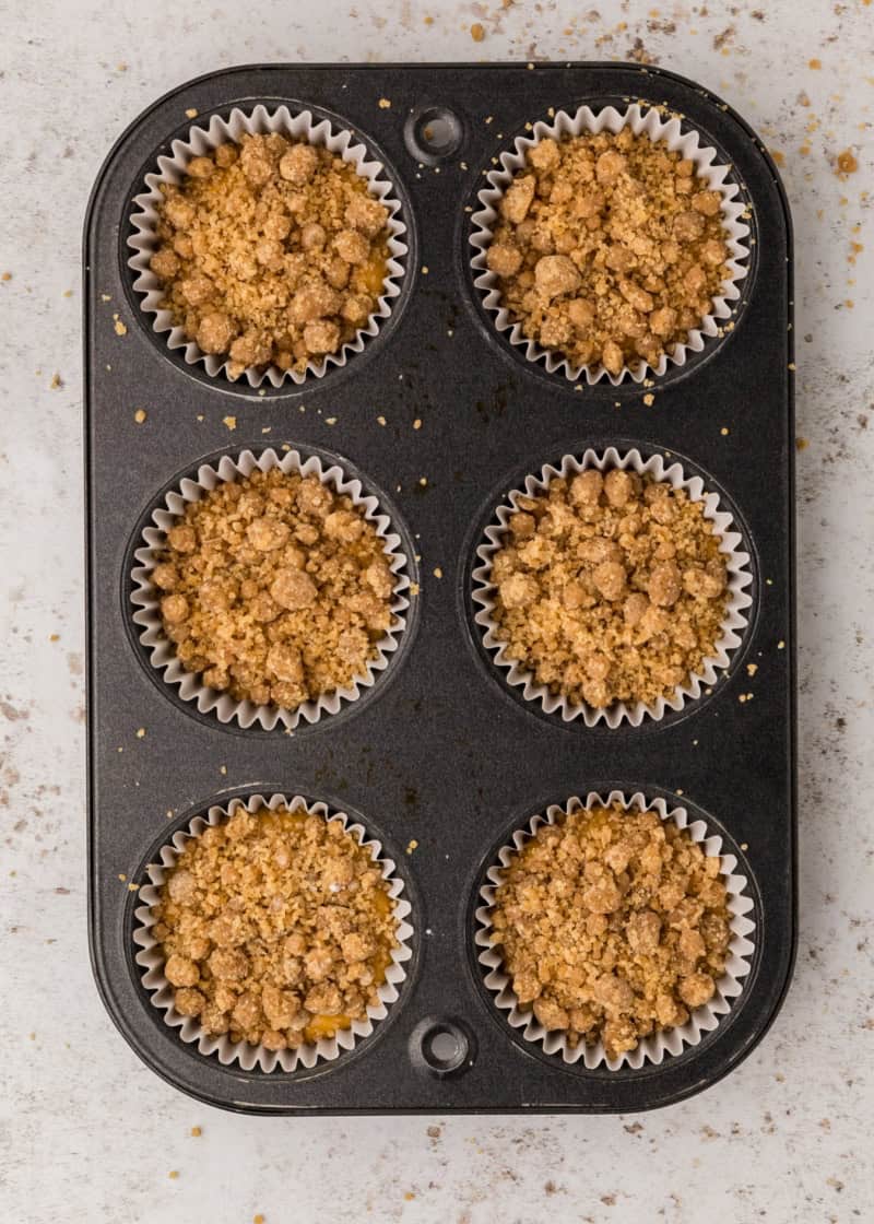 A muffin pan filled with uncooked crumbly topped muffins.