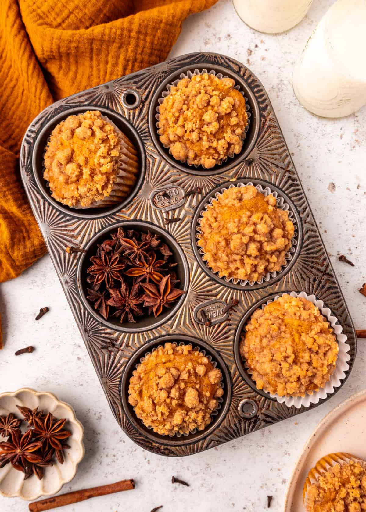 Pumpkin Streusel Muffins in a muffin tin on a table with a jug of milk.