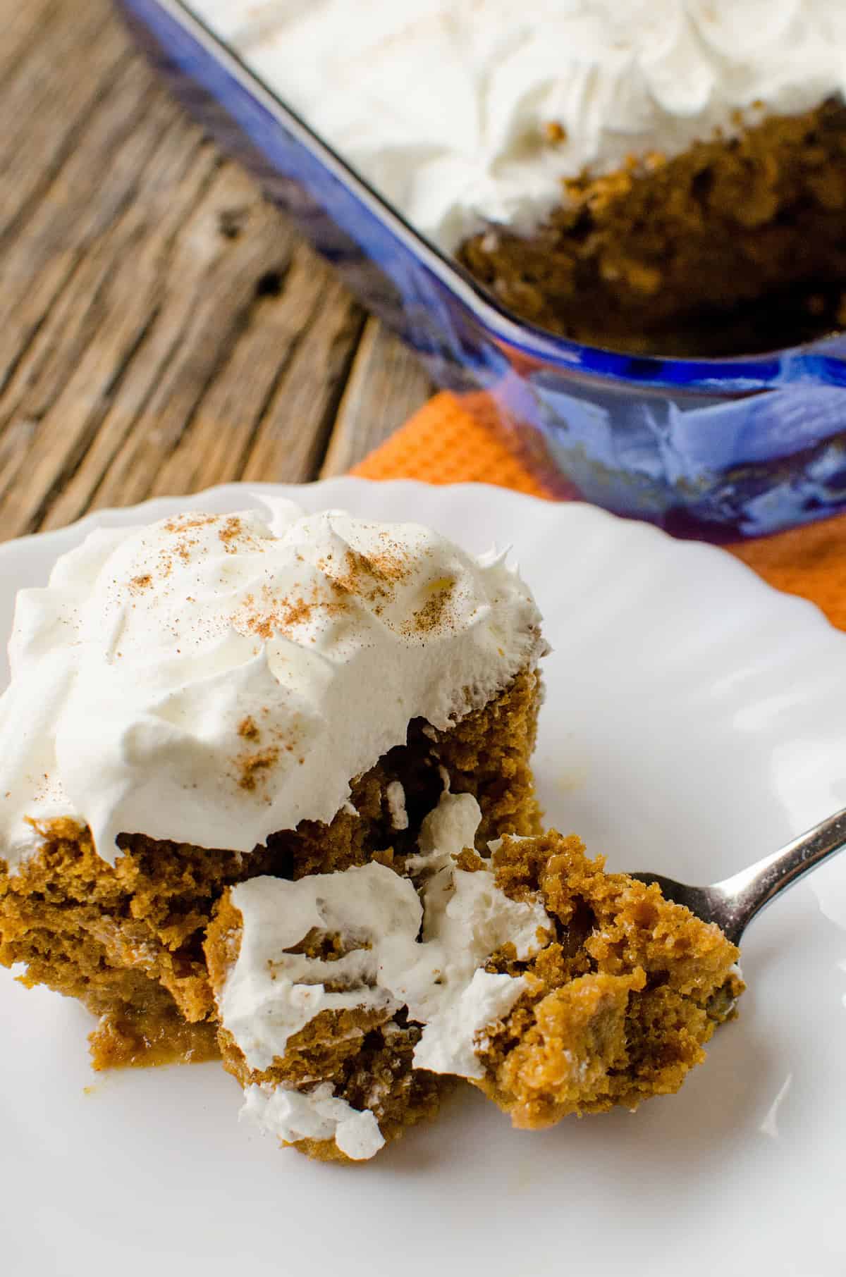 a slice of Pumpkin Spice Poke Cake on a white plate with a fork.