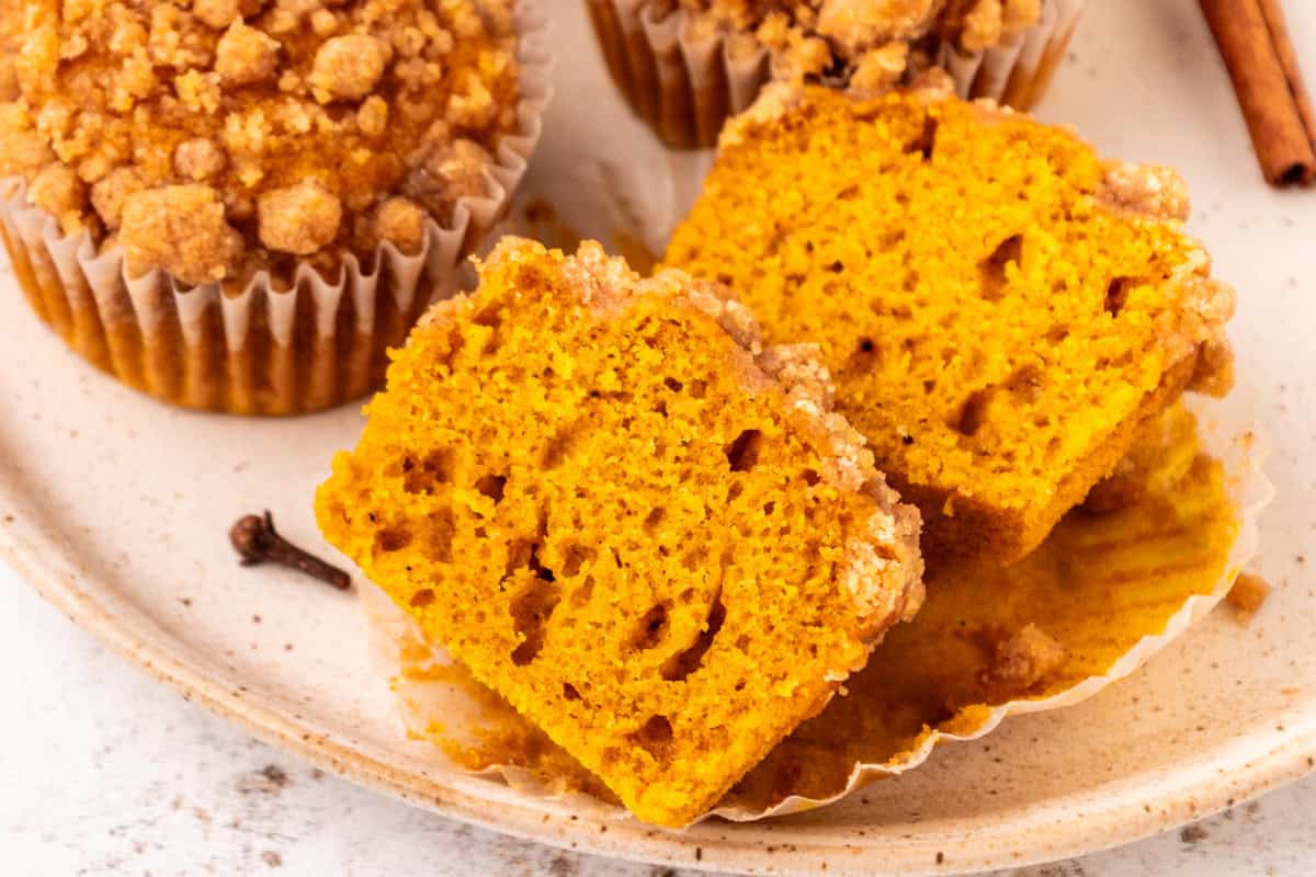 Pumpkin crumb muffins on a plate with one cut open.