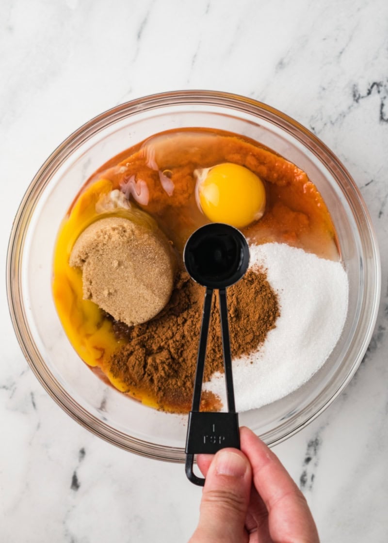 ingredients to make pumpkin dump cake recipe in a glass bowl with vanilla extract.