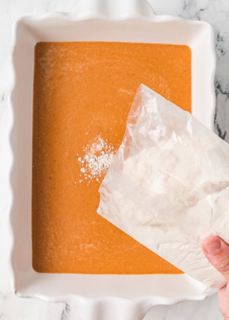 dry cake mix being sprinkled on top of pumpkin cake batter.