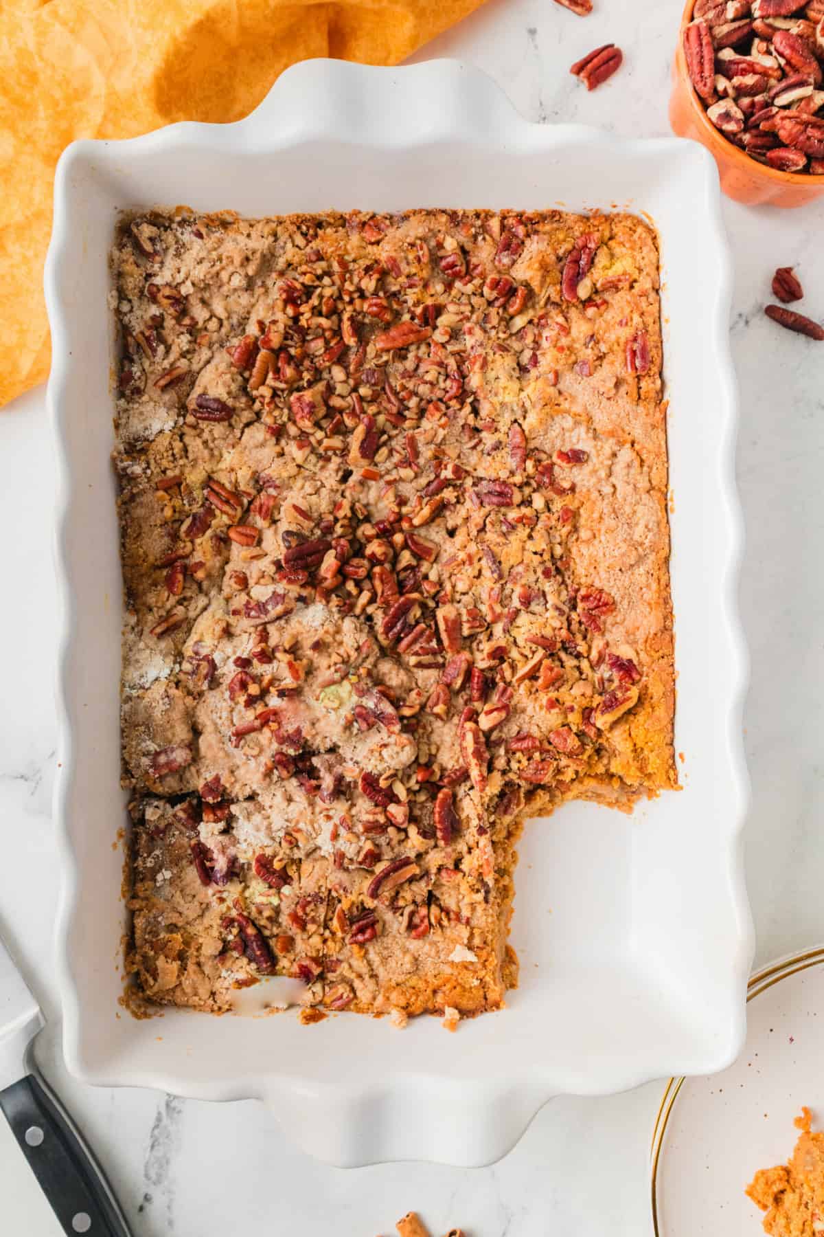 Pumpkin dump cake with pecans on top, in a white baking dish, with a piece taken out.