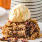 A piece of pumpkin dump cake on a plate with a scoop of ice cream on top.