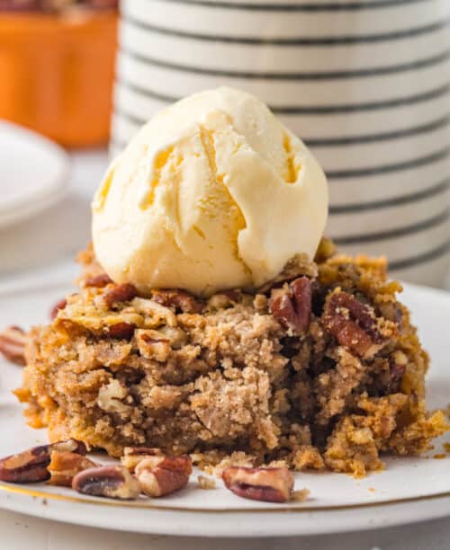 A piece of pumpkin dump cake on a plate with a scoop of ice cream on top.