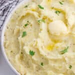 Boursin mashed potatoes with butter and chopped parsley on top in a bowl.