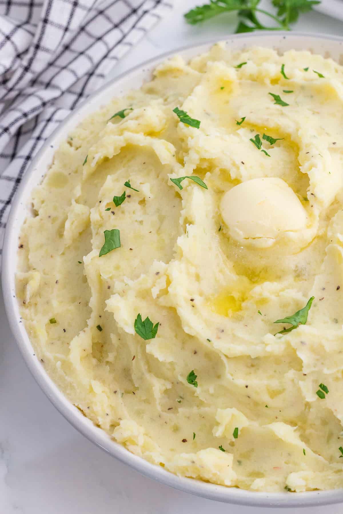 Boursin mashed potatoes with butter and chopped parsley on top in a bowl.