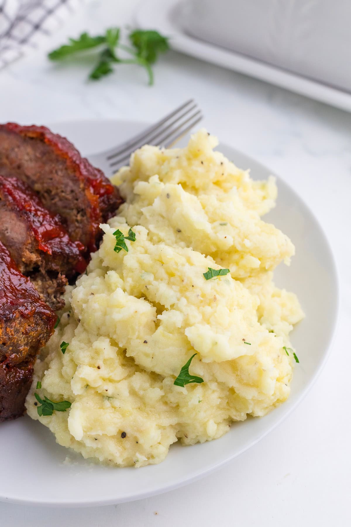 A white plate with meat and buttery mashed potatoes with Boursin cheese and fresh parsley.