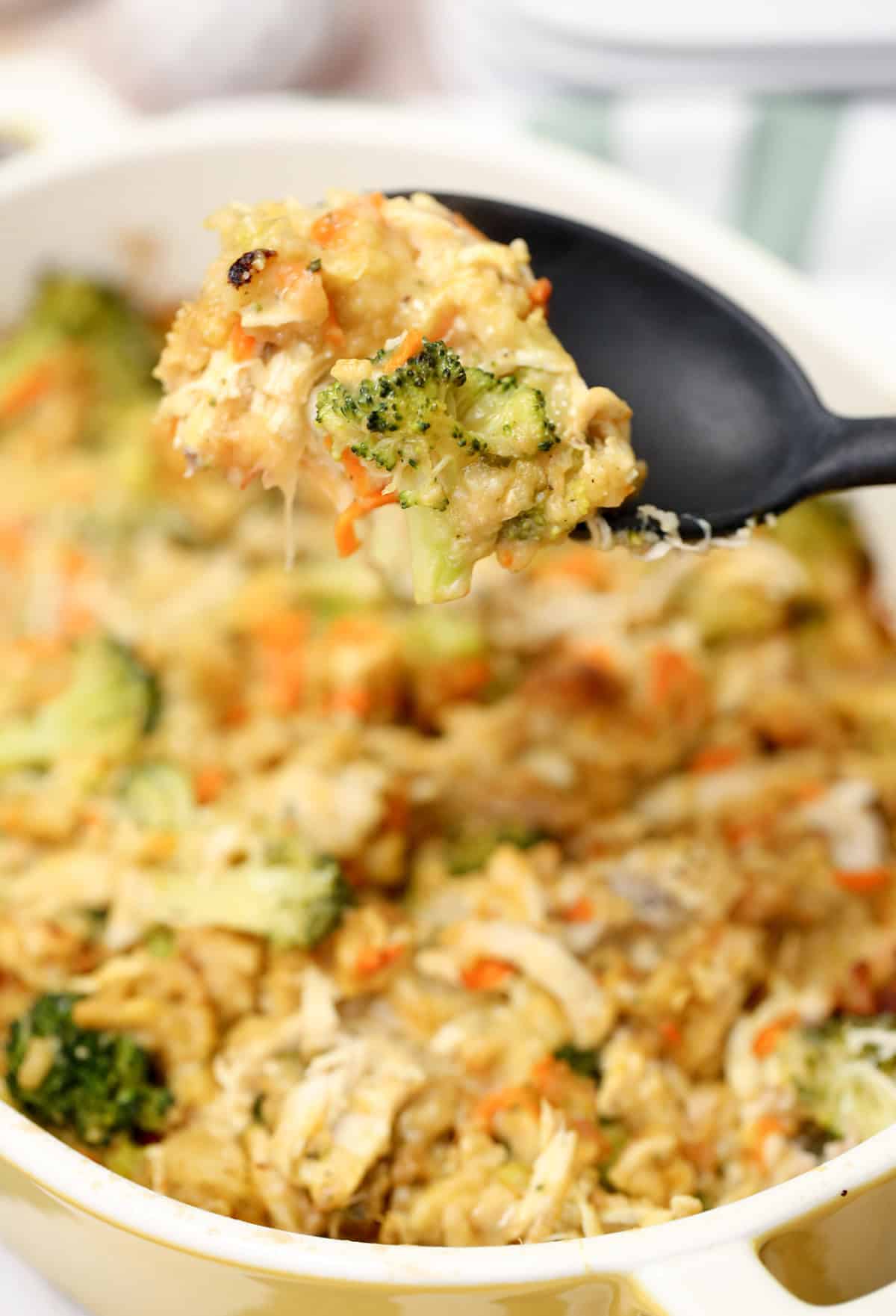 A serving spoon with chicken and stuffing casserole on it, over a baking dish full.