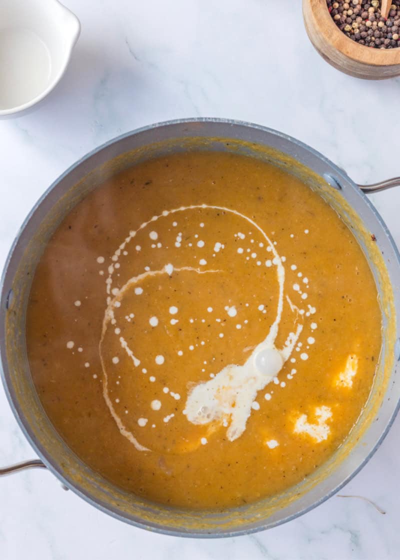 a pot of Apple Butternut Squash Soup cooking pot with cream drizzled on top.