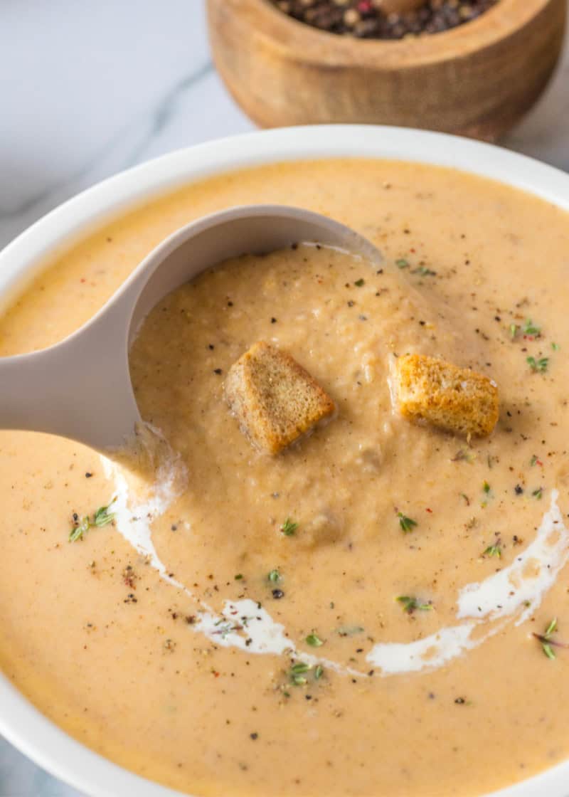 Creamy homemade Butternut Squash Soup with Apple in a white bowl with bread croutons, fresh herbs, and black pepper.