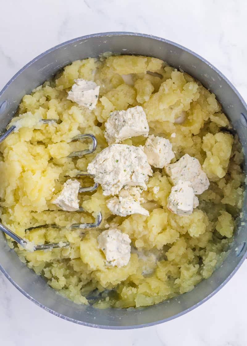 Boursin cheese added to mashed potatoes in a pot.