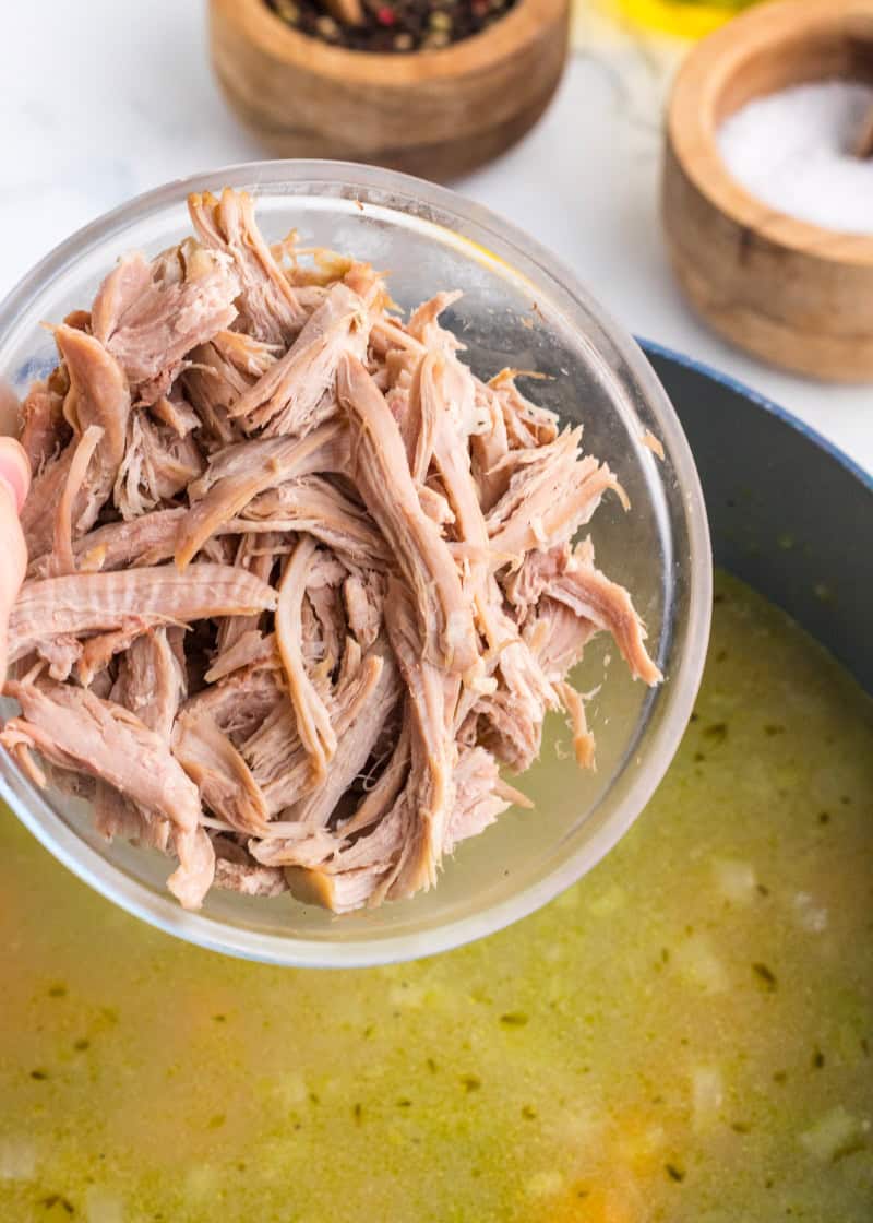shredded turkey being poured into a pot of soup.