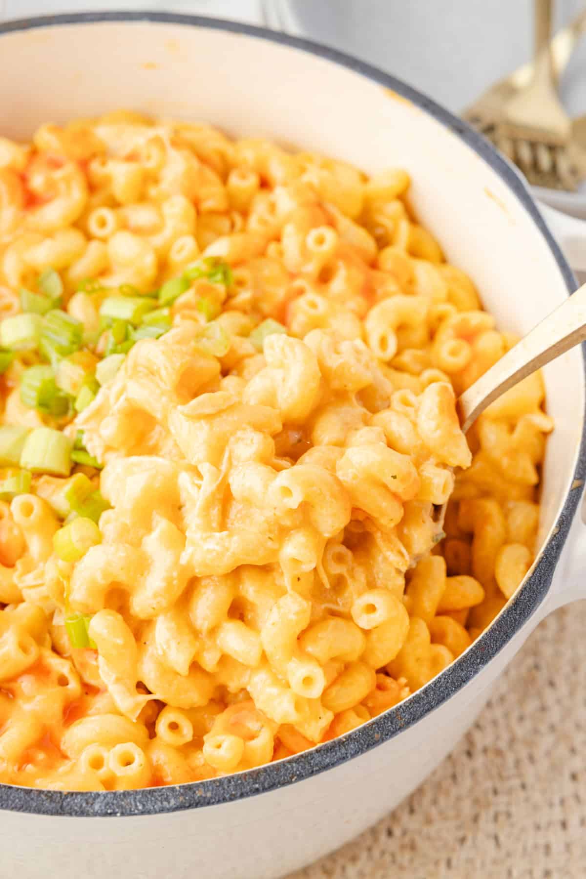 buffalo chicken mac and cheese in a pot with chopped green onions on top, and some being picked up by a serving spoon.