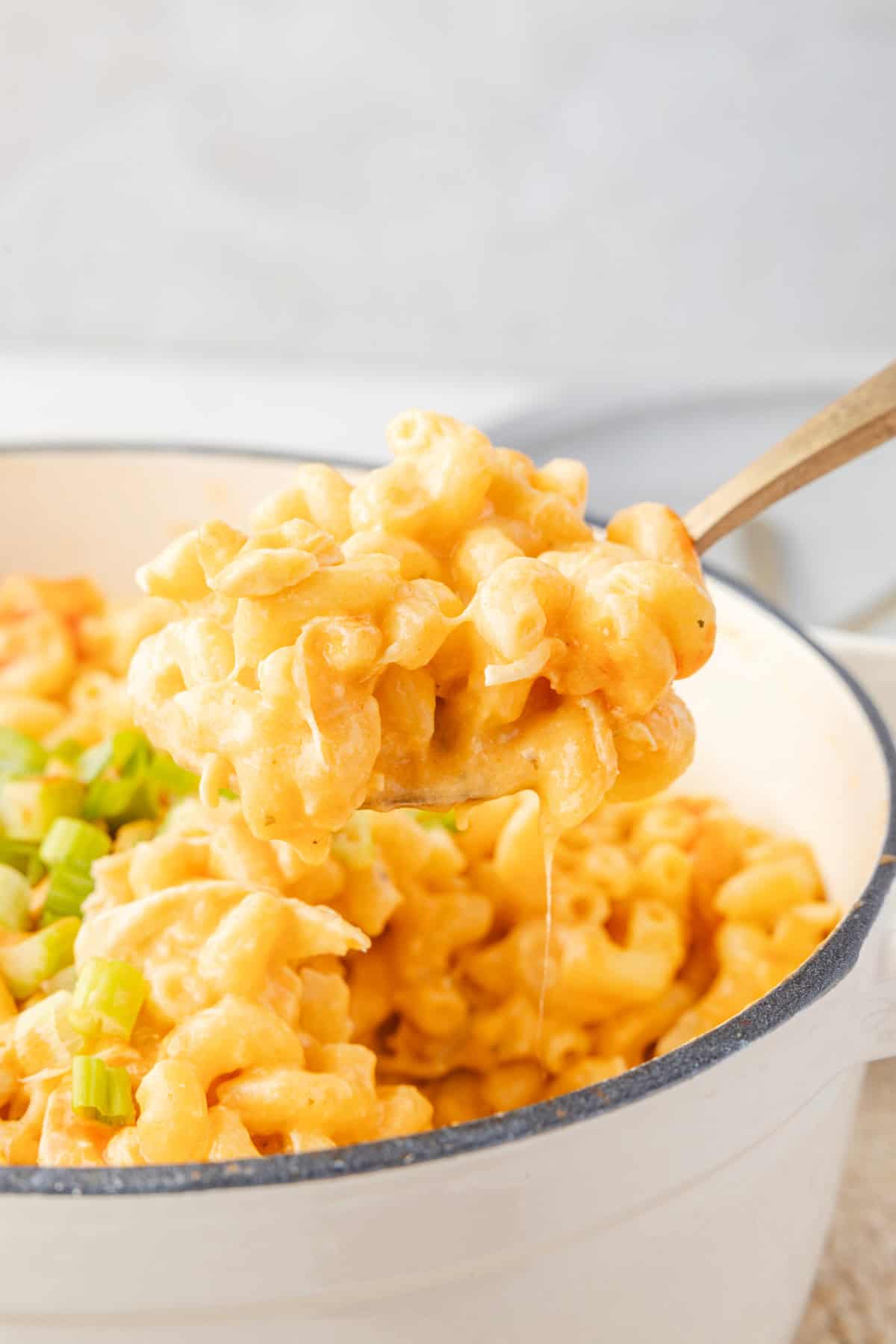 buffalo chicken mac and cheese in a pot with chopped green onions on top, and some being picked up by a serving spoon.