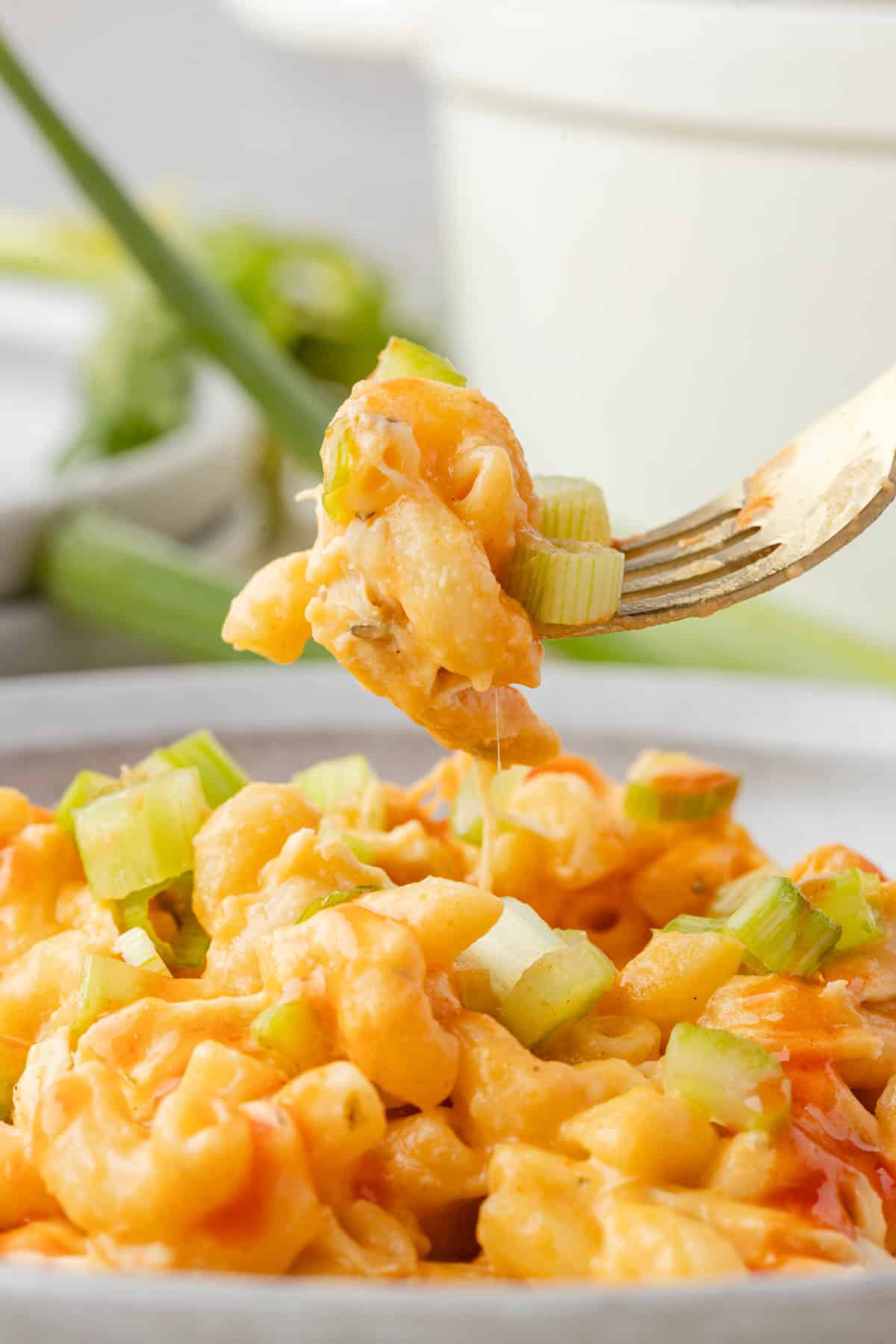 buffalo chicken mac and cheese in a bowl with chopped green onions on top, and some being picked up by a fork.