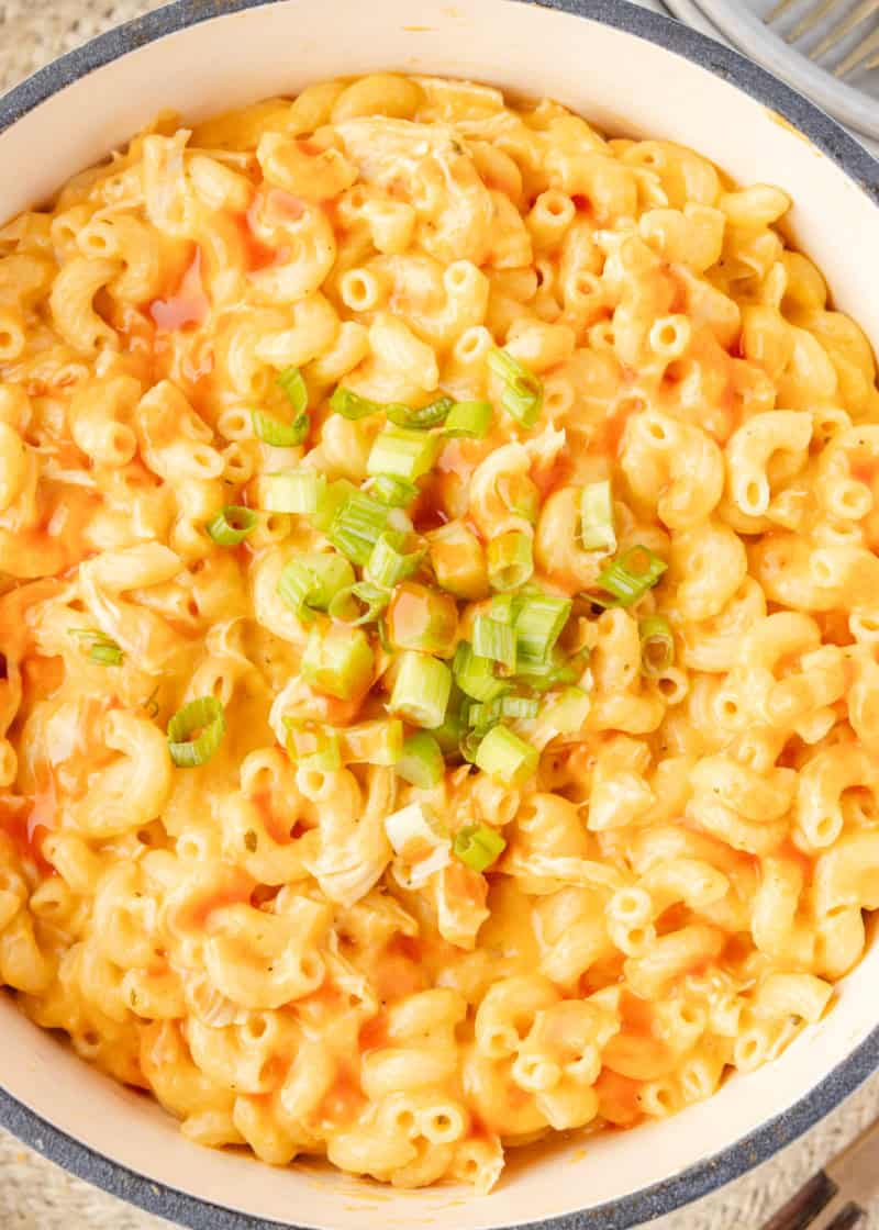 Creamy macaroni and cheese with green onions in a pot.