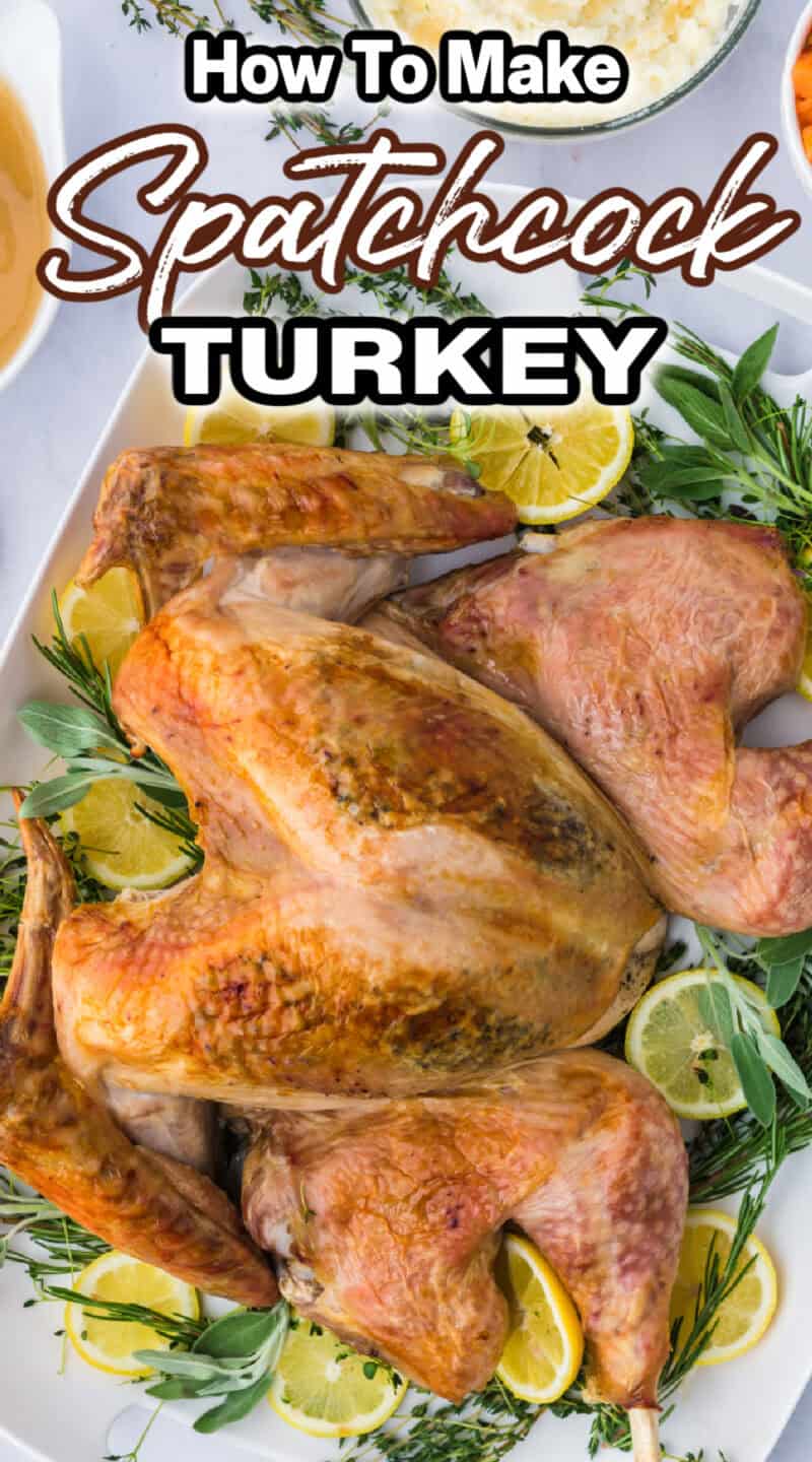 a whole roasted spatchcock turkey on a platter with fresh herbs and lemon slices.