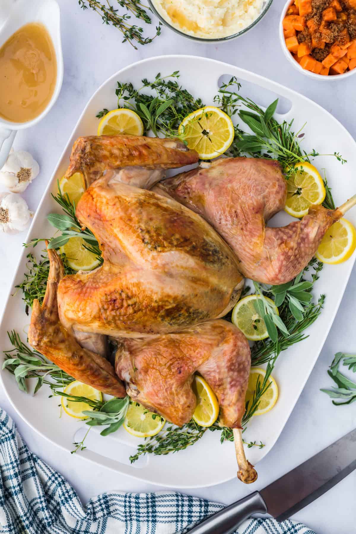 a whole roasted spatchcock turkey on a platter with fresh herbs and lemon slices.