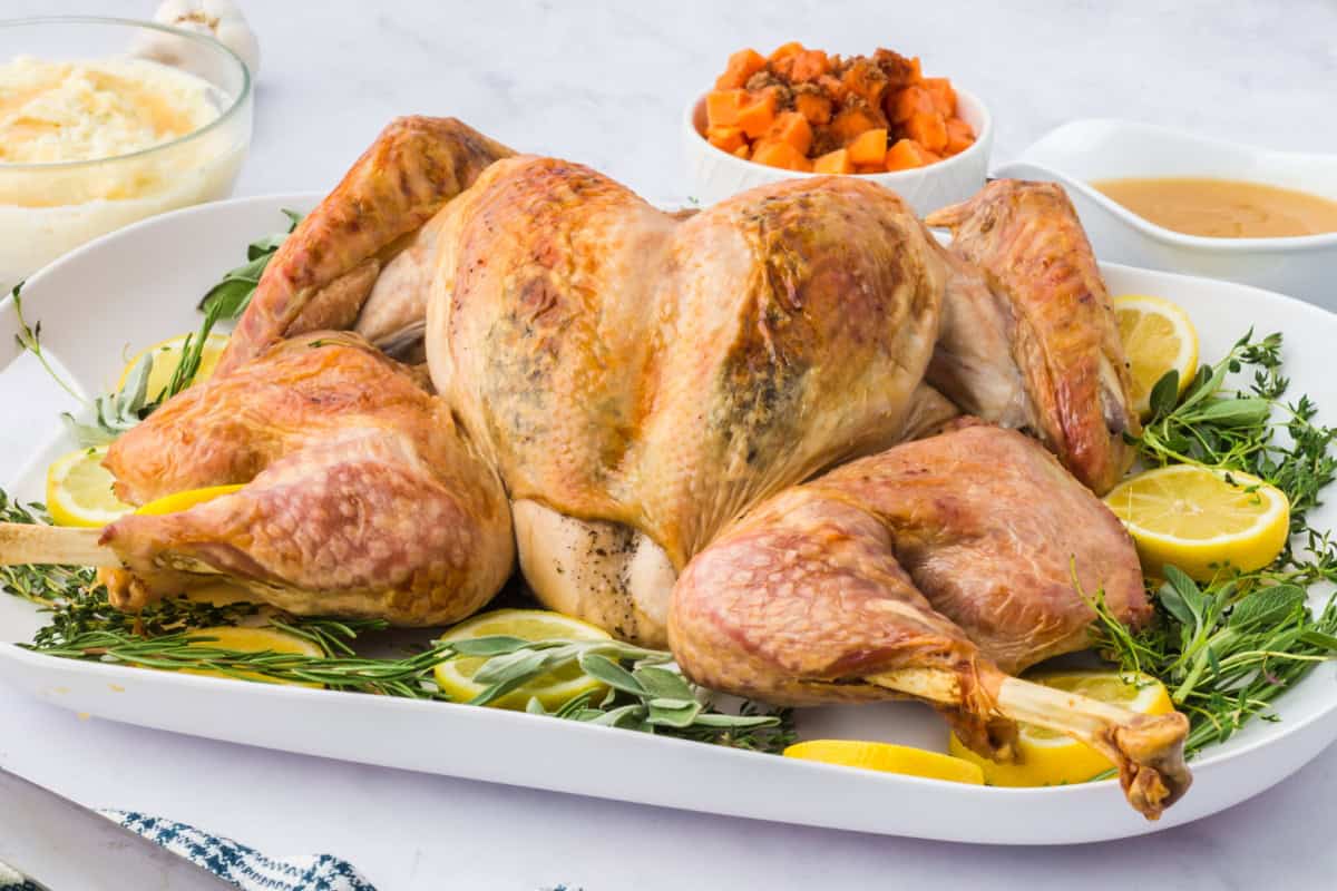 a whole roasted spatchcock turkey on a platter with fresh herbs and lemon slices.