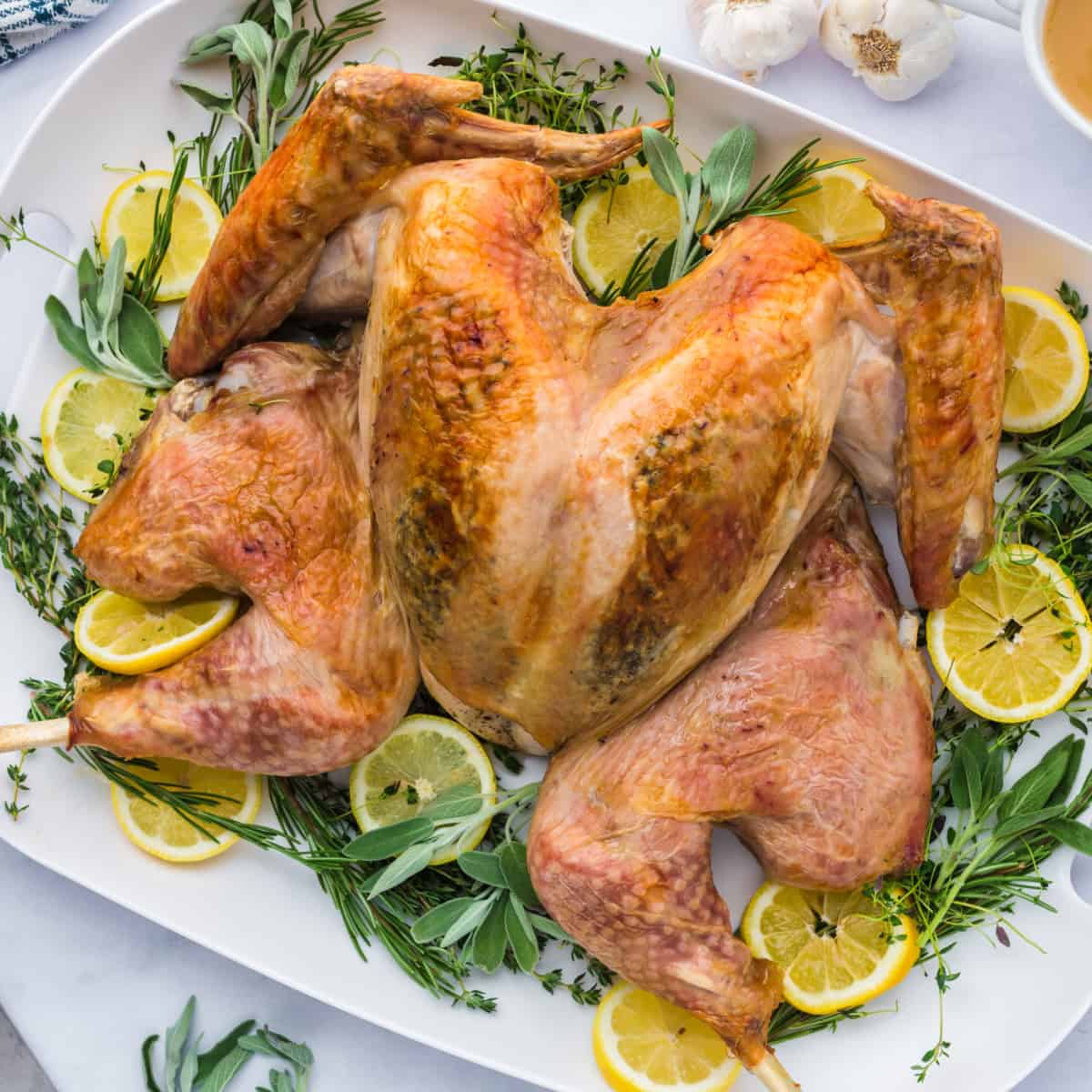 a whole roasted spatchcock turkey on a platter with fresh herbs and lemon slices.
