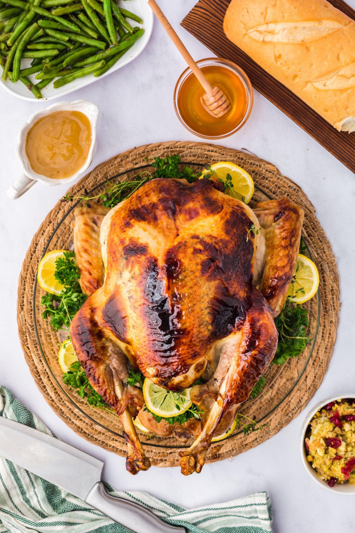 whole cooked honey glazed turkey on a table surrounded by honey, gravy, green beans, and bread.