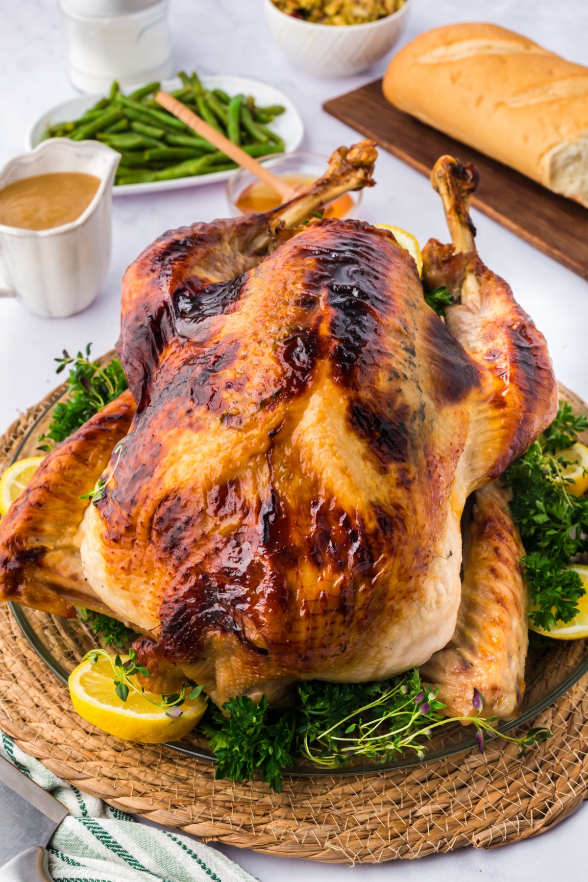 whole cooked honey glazed turkey on a table surrounded by honey, gravy, green beans, and bread.