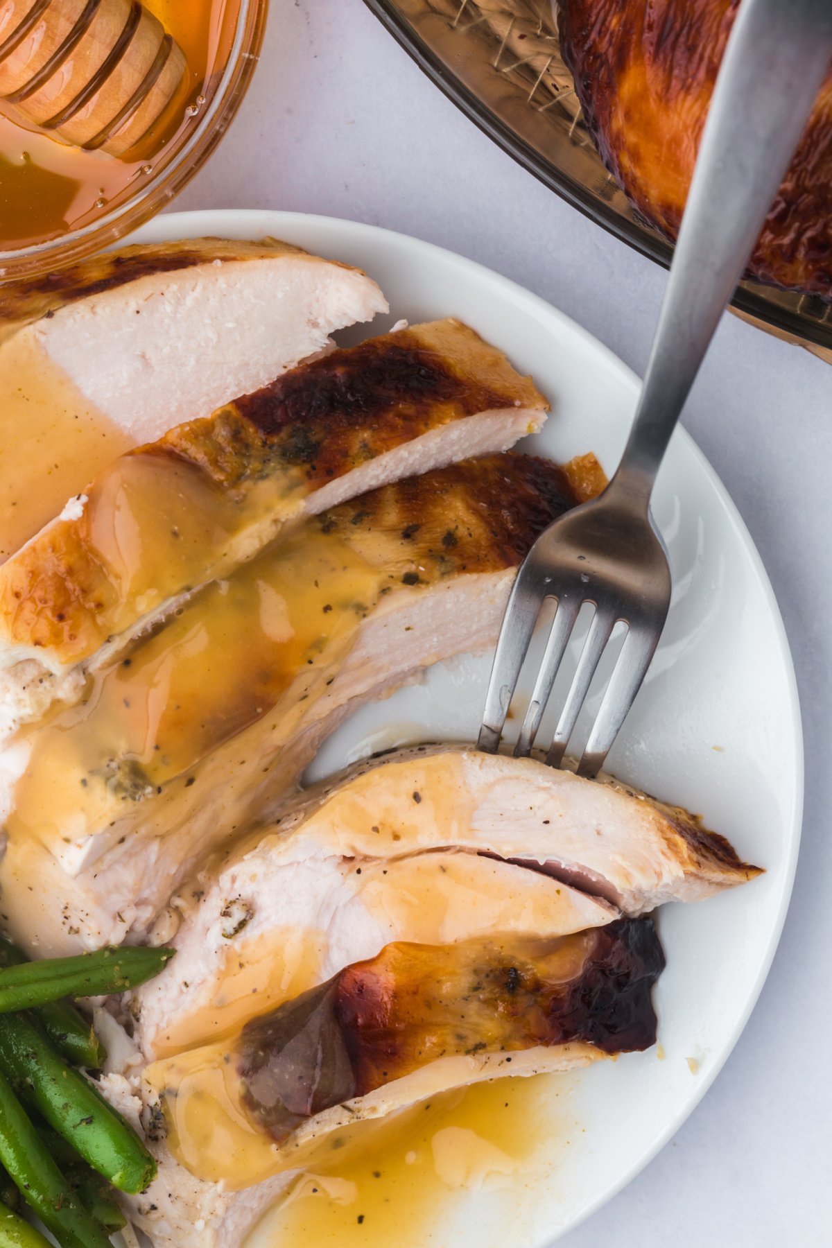sliced honey glazed turkey on a plate with gravy and green beans.