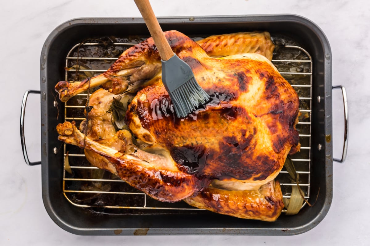 Cooked honey glazed turkey in a roasting pan being glazed.