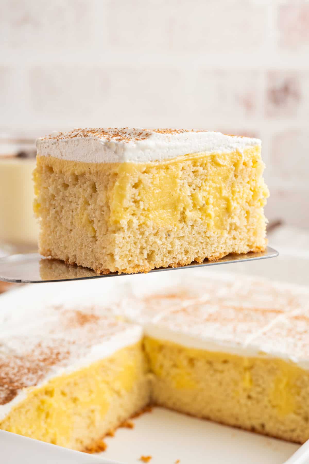 a spatula picking up a slice of eggnog poke cake from a whole cake.