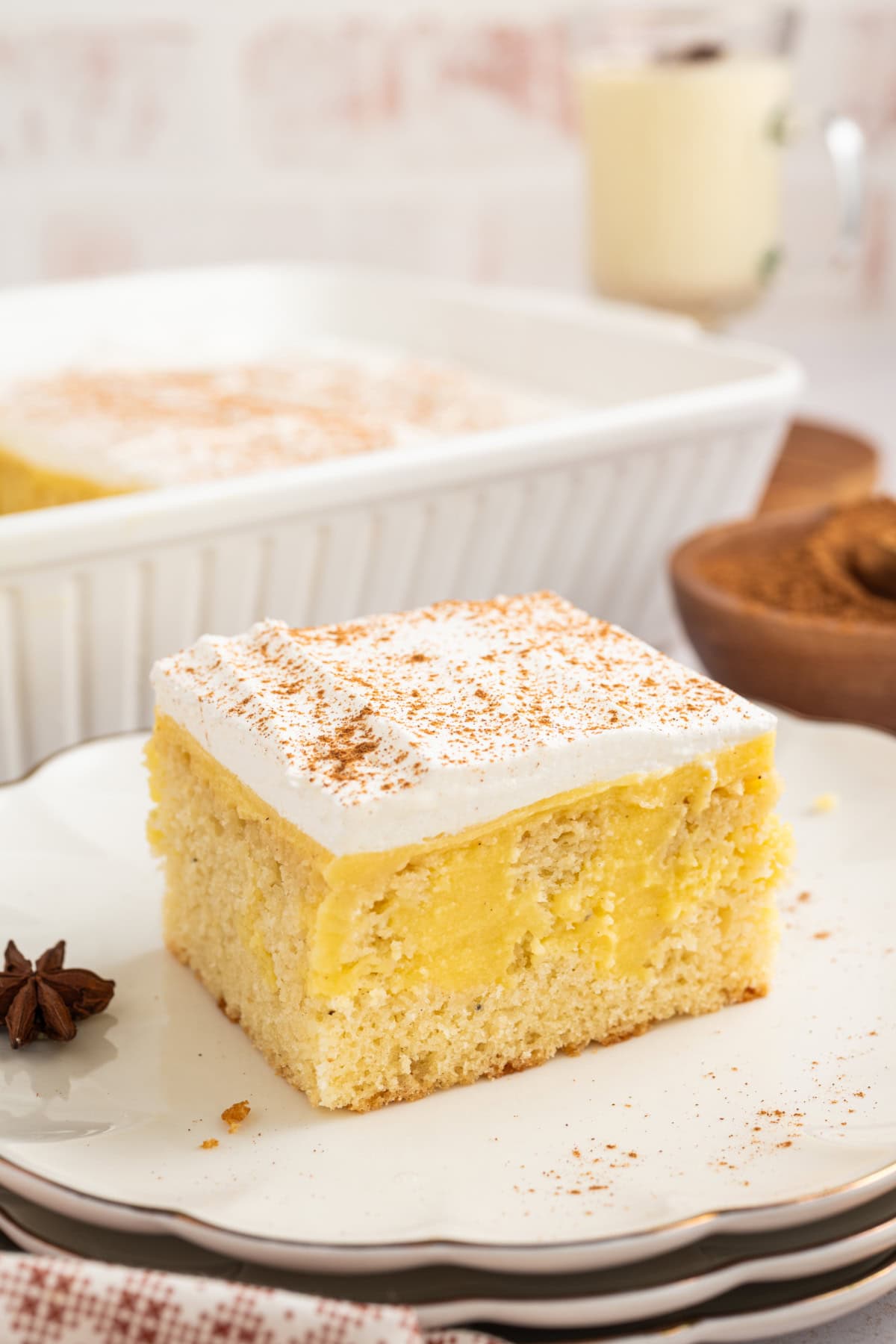 a slice of eggnog poke cake on a plate next to the whole cake.