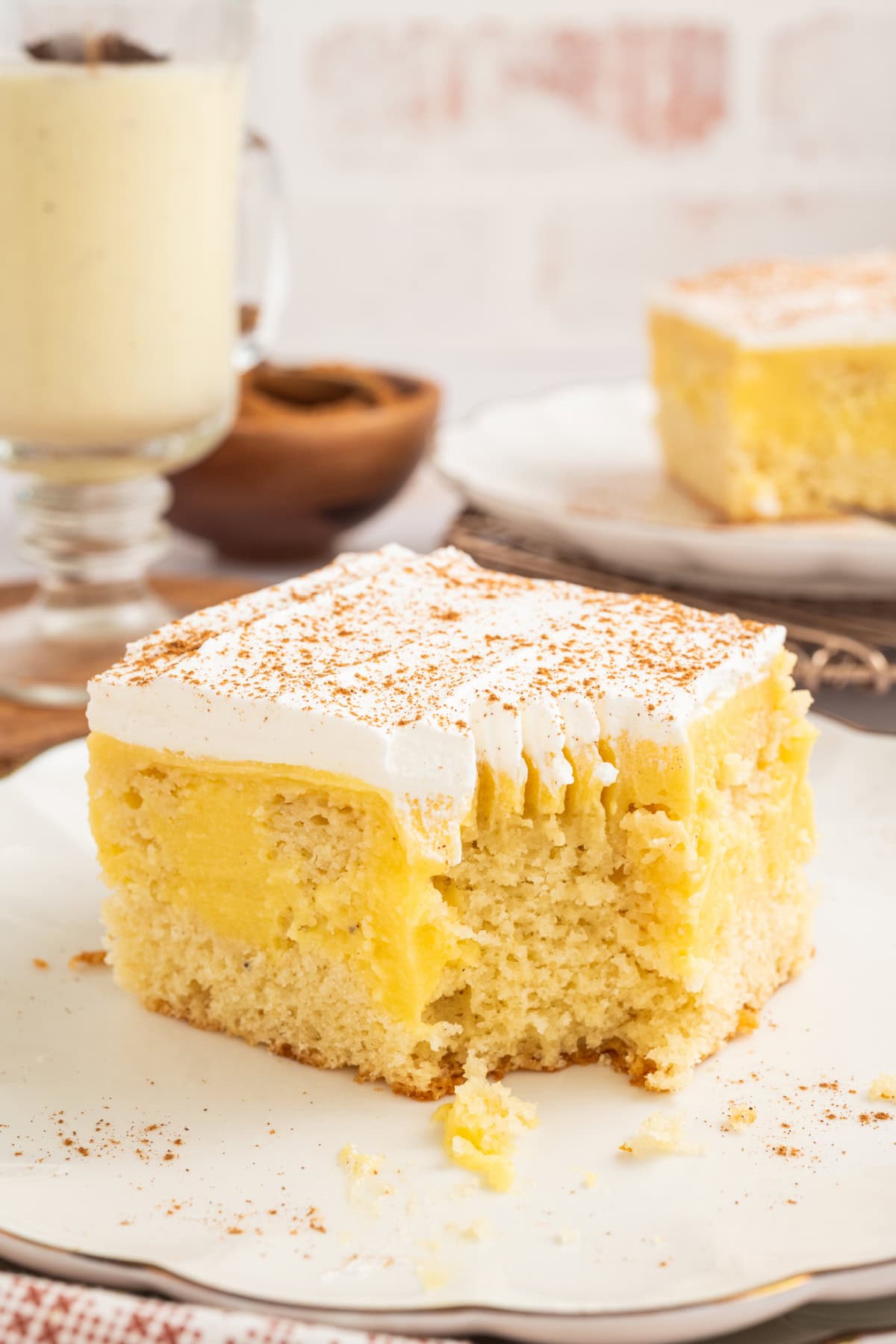a slice of eggnog poke cake with whipped topping and cinnamon on top, on a plate.