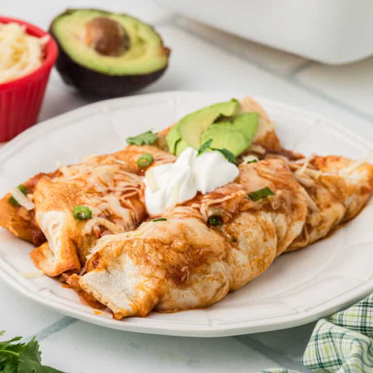 Turkey Enchiladas on a plate with sour cream and avocado slices on top.