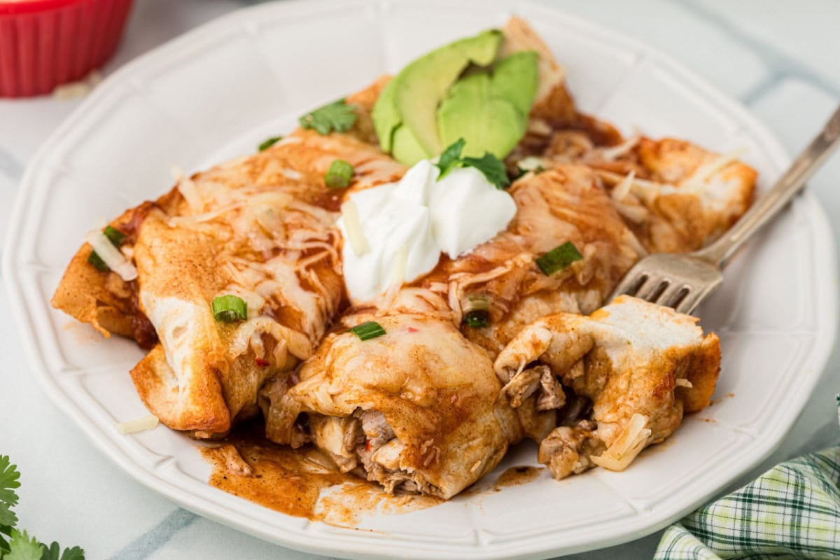 Turkey Enchiladas on a plate with a fork, with sour cream and avocado slices on top.