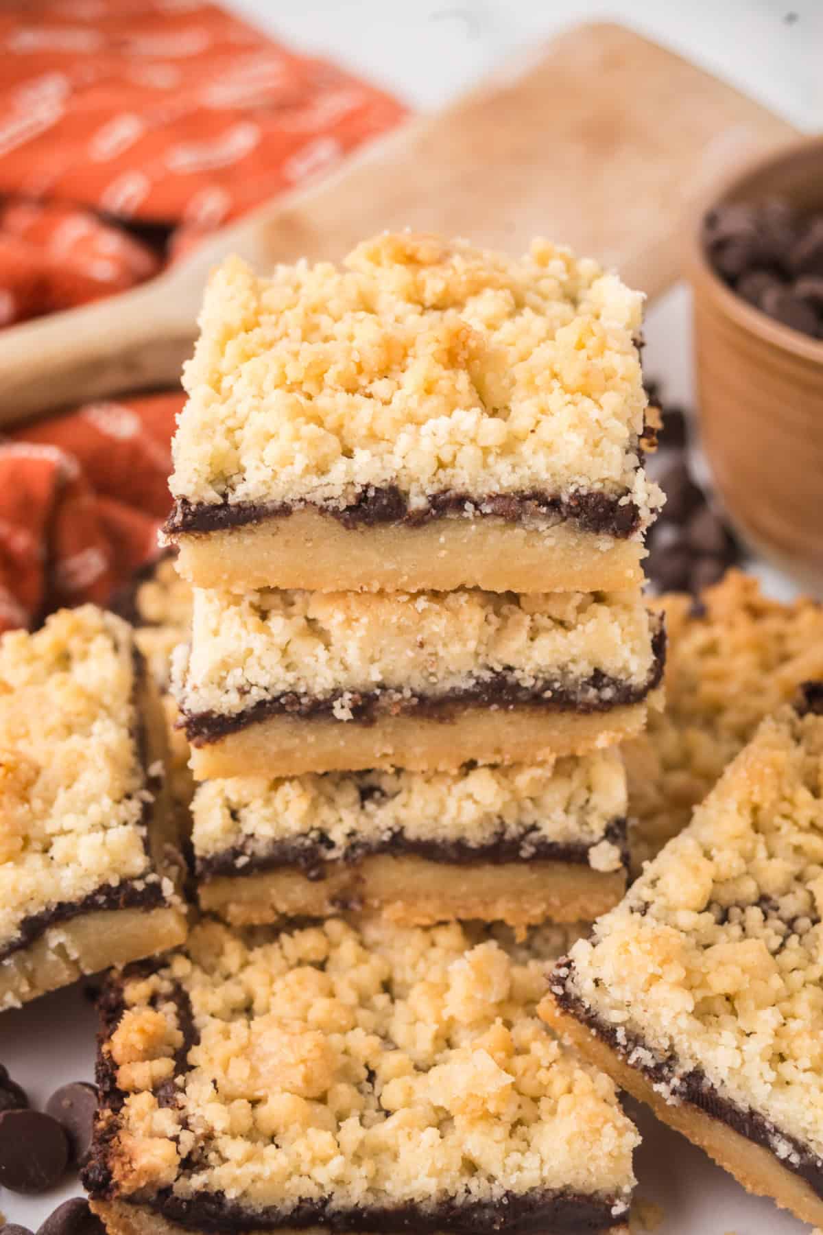 A pile of Chocolate Shortbread Bars beside a bowl of chocolate chips and a wooden spoon.