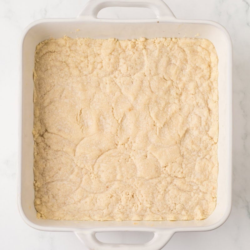 Shortbread pressed into the bottom of a white square baking pan.