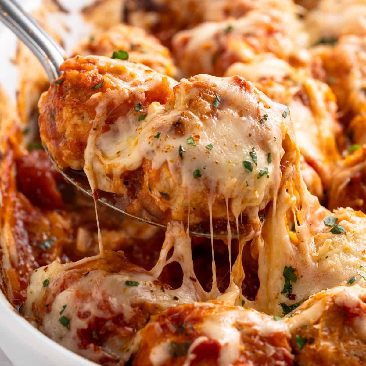 chicken parmesan meatballs in a baking dish with melted cheese on top with a spoon.