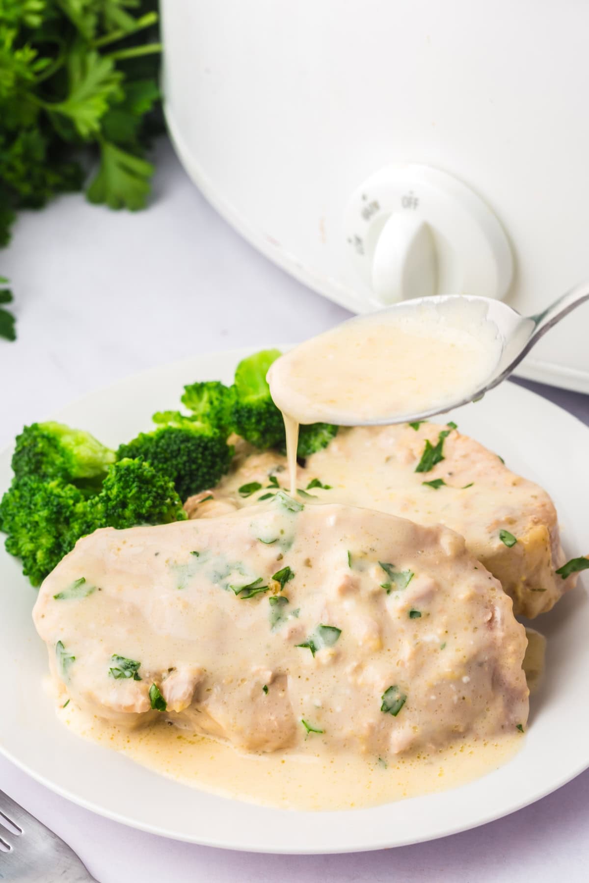 Creamy ranch sauce being spooned onto cooked pork chops made in the crockpot.