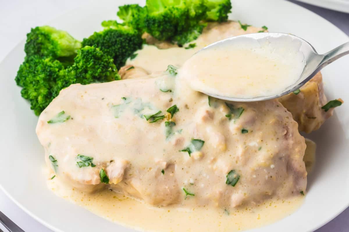 Creamy Ranch sauce being spooned onto pork chops made in the crockpot. garnished with parsley.
